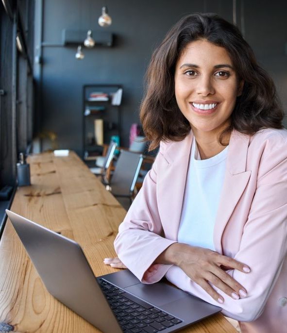 Jeune professionnelle souriante travaillant sur un ordinateur portable dans un espace moderne, illustrant la formation continue à l’UdeM pour professionnels formés à l'étranger et résidents permanents.