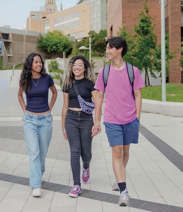 Trois jeunes élèves du secondaire, deux femmes et un homme, marchent ensemble en souriant et en échangeant sur le campus de l'Université de Montréal.